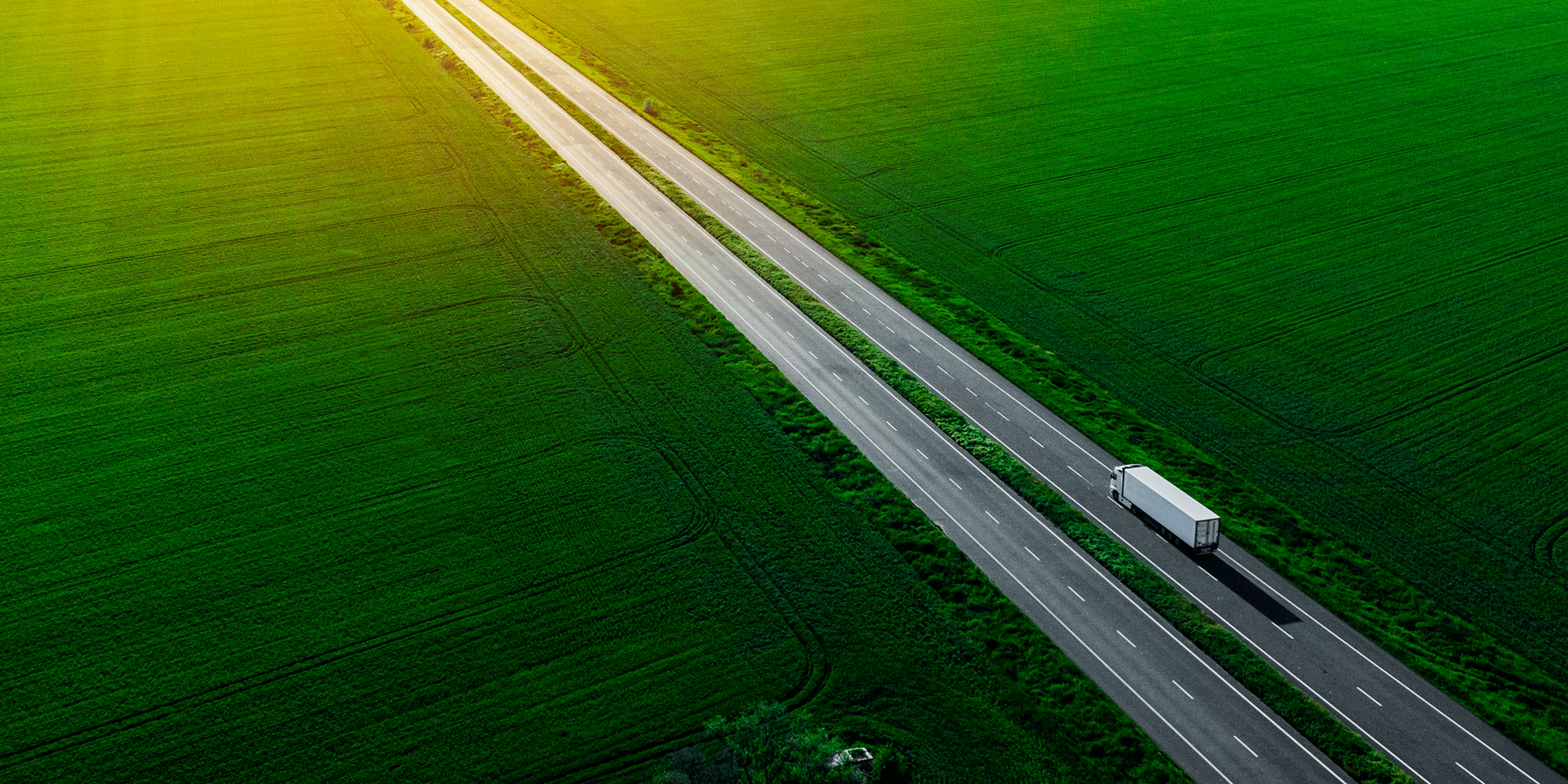 Lorry driving on a road in between green fields